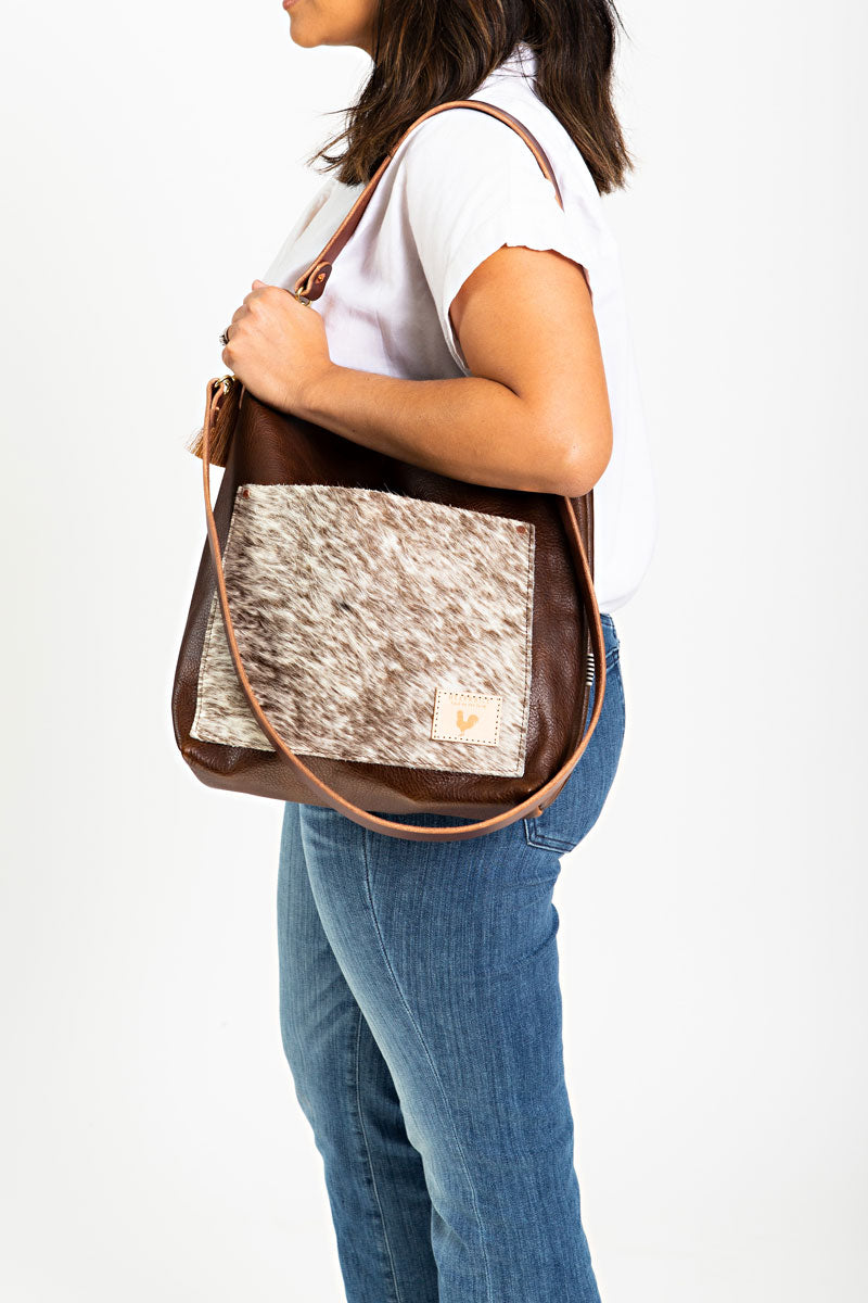 A woman wearing the hair on hide bag with brown straps and the meanwhile logo.