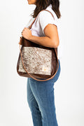 A woman wearing the hair on hide bag with brown straps and the meanwhile logo.
