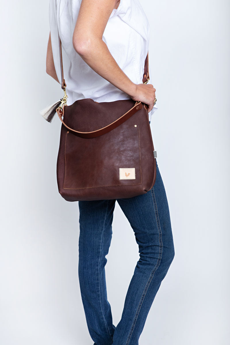 A woman holding the mocha brown bag with body strap and the meanwhile logo.