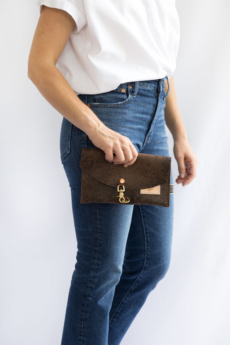 Woman holding a birch mocha bag with a hook clasp and meanwhile logo. 