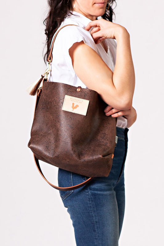 A women holding the birch mocha brown bag with a brown tassel and body strap.