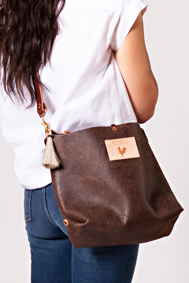 Woman wearing the birch mocha bag with dark brown cross body strap, meanwhile logo, and a light tan tassel.