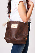 A women holding the birch mocha brown bag with a tan tassel and body strap.