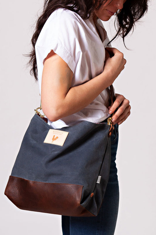 A woman wearing the slate grey bag with a dark brown body strap and meanwhile logo. 