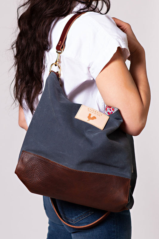 A woman wearing the slate grey bag with a dark brown body strap and meanwhile logo. 