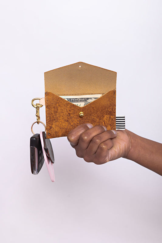 A hand holding a brown wallet with a light pink tag to clip keys onto the side.