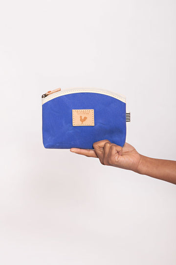A hand holding the royal blue makeup bag with a light brown zipper and a white trim at the top.