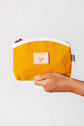 Hand holding small mustard colored zippered bag with cream colored accent around zipper