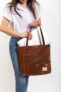 Woman placing her laptop in a dark brown bag with meanwhile logo and shoulder straps.