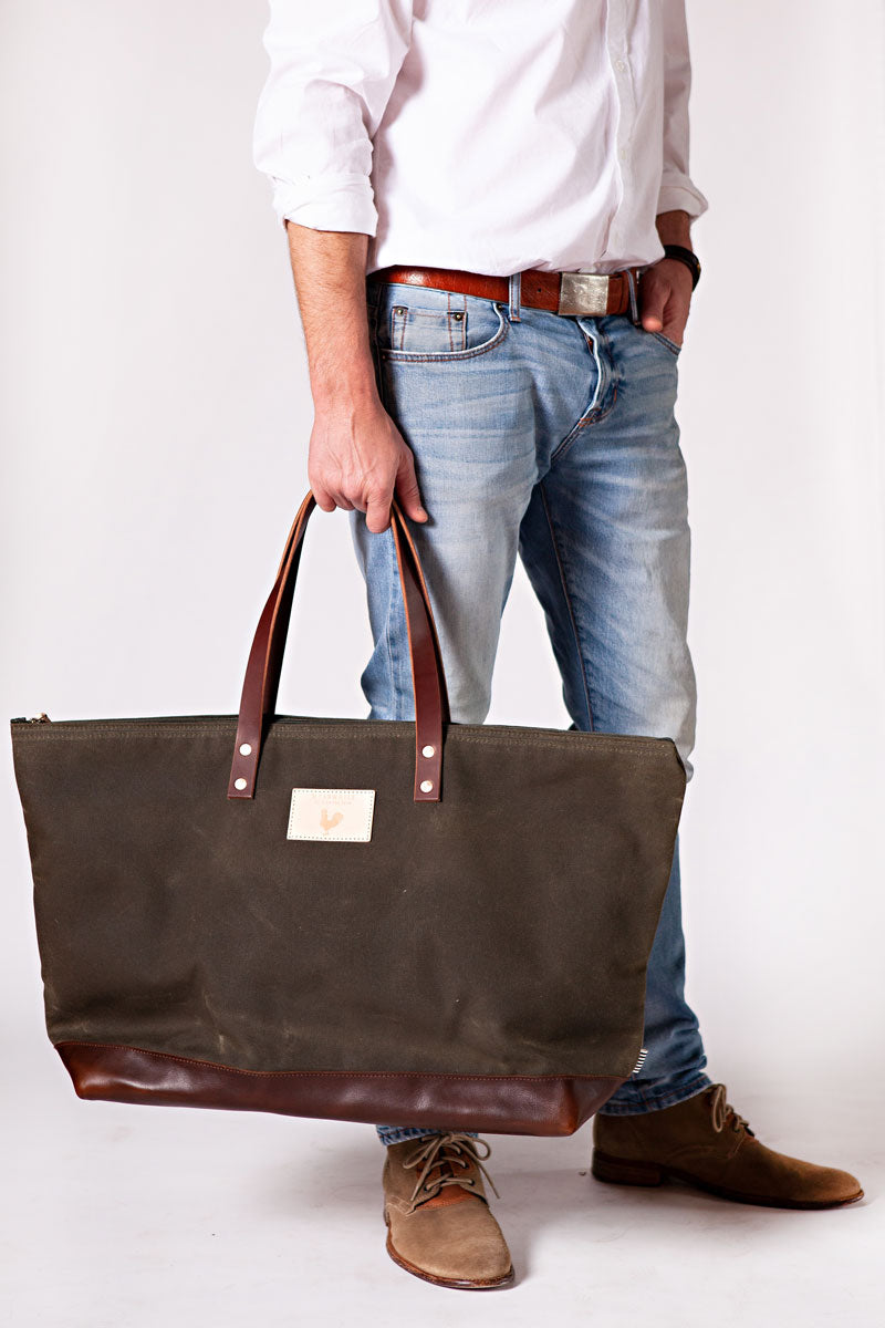 A man holding the olive green weekend bag with the meanwhile logo and dark brown shoulder straps.