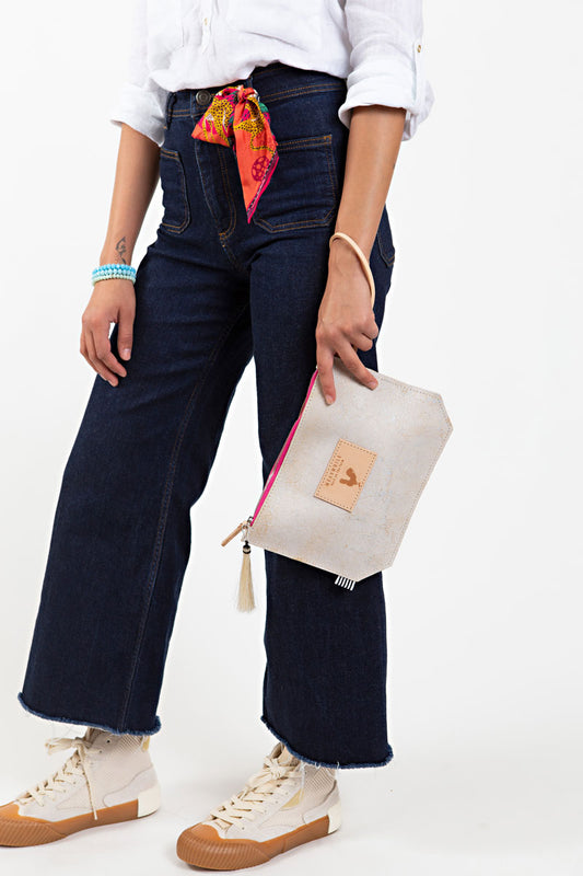 A woman holding the birch white wristlet bag with bright pink at the zipper, tan tassel, and meanwhile logo. 